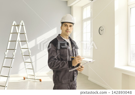 Contractor in safety helmet with clipboard assessing light modern home interior Contractor in safety helmet with clipboard assessing light modern home interior 142893048