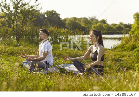 Yogi people sitting in lotus pose outdoors on green grass, meditating, calming activity Yogi people sitting in lotus pose outdoors on green grass, meditating, calming activity 142893167