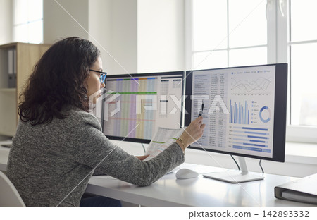 Accountant analyzing financial data on multi monitor workstation in modern office Accountant analyzing financial data on multi monitor workstation in modern office 142893332