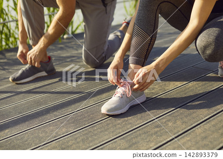 Sporty people bending down, actively tying shoelaces close up preparing for sport activity, running Sporty people bending down, actively tying shoelaces close up preparing for sport activity, running 142893379