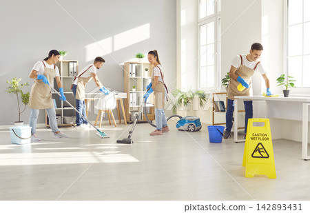Happy smiling young cleaners men and women in uniform wiping desk, mopping floor and vacuuming. Happy smiling young cleaners men and women in uniform wiping desk, mopping floor and vacuuming. 142893431