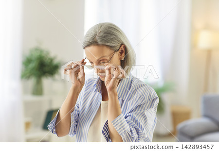 Concentrated senior aged female wearing glasses, pleasant confident old age woman at home Concentrated senior aged female wearing glasses, pleasant confident old age woman at home 142893457