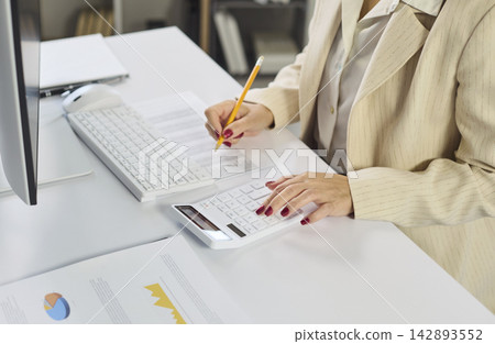 Female accountant using calculator and keyboard for budgeting and finance in office Female accountant using calculator and keyboard for budgeting and finance in office 142893552