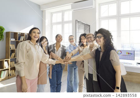 Business women stacking hands in office, celebrating teamwork, unity and success Business women stacking hands in office, celebrating teamwork, unity and success 142893558