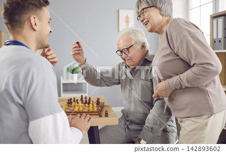 Young nurse man playing chess game with happy smiling senior elderly couple in clinic. Young nurse man playing chess game with happy smiling senior elderly couple in clinic. 142893602