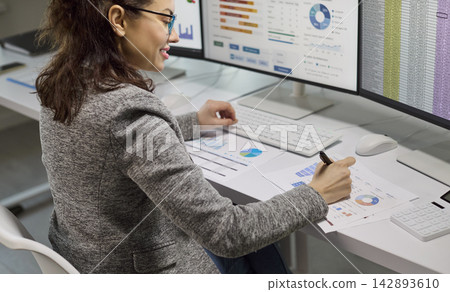 Female accountant analyzing financial data on computer monitors with spreadsheets Female accountant analyzing financial data on computer monitors with spreadsheets 142893610