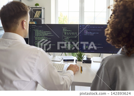 Developers collaborating on code at dual monitors in office, programming team Developers collaborating on code at dual monitors in office, programming team 142893624