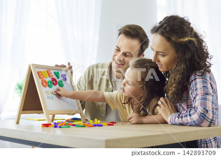 Parents guide daughter learning alphabet on magnetic board at home together Parents guide daughter learning alphabet on magnetic board at home together 142893709