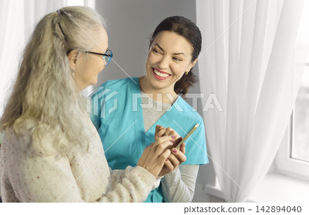 Smiling nurse helps senior woman with smartphone during friendly home care visit Smiling nurse helps senior woman with smartphone during friendly home care visit 142894040