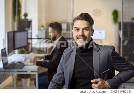 Smiling confident businessman portrait in modern office with coworker at computer Smiling confident businessman portrait in modern office with coworker at computer 142894058
