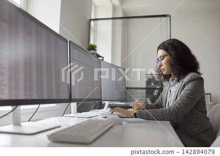 Accountant analyzing spreadsheets on multiple monitors in office finance audit Accountant analyzing spreadsheets on multiple monitors in office finance audit 142894079