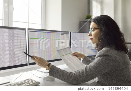 Woman accountant analyzing spreadsheets and reports on three computer monitors Woman accountant analyzing spreadsheets and reports on three computer monitors 142894404