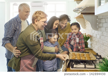 Happy multigenerational family taking cookies from oven in cozy home kitchen Happy multigenerational family taking cookies from oven in cozy home kitchen 142894430