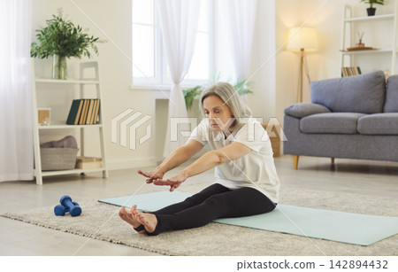 Yogi fit old sporty senior woman practicing yoga home, sitting doing stretching exercise, relax pose Yogi fit old sporty senior woman practicing yoga home, sitting doing stretching exercise, relax pose 142894432