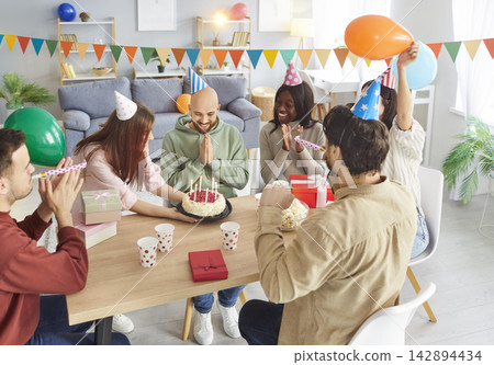 Happy people congratulating a young friend sitting at festive table on birthday party at home. Happy people congratulating a young friend sitting at festive table on birthday party at home. 142894434