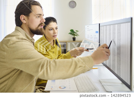 Couple analyzing spreadsheet for budget at home, planning savings on large monitor Couple analyzing spreadsheet for budget at home, planning savings on large monitor 142894523