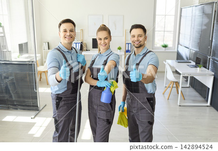 Happy cleaning crew in uniforms showing thumbs up gesture in modern office Happy cleaning crew in uniforms showing thumbs up gesture in modern office 142894524