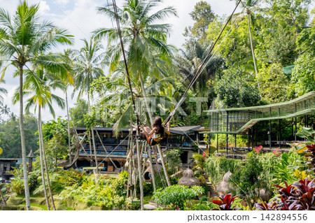 Tourists riding a giant swing in a tropical jungle surrounded by coconut palms. Tourists riding a giant swing in a tropical jungle surrounded by coconut palms. 142894556