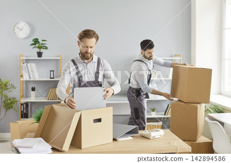 Service team men packing boxes, placing items inside, lifting stacking containers, focused moving Service team men packing boxes, placing items inside, lifting stacking containers, focused moving 142894586