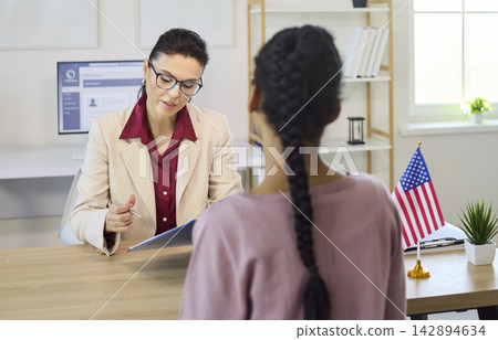 Immigration consultant interviewing client about visa documents in office with flag 142894634