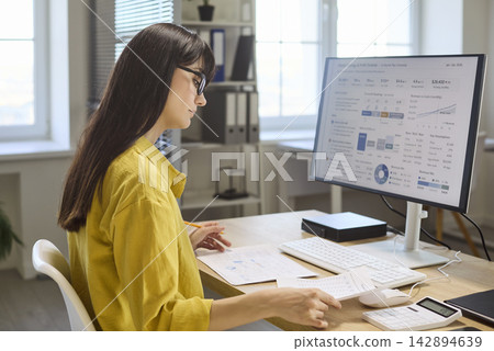 Woman accountant analyzing finance charts at computer with papers and calculator 142894639