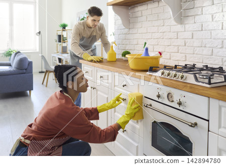 Young couple cleaning kitchen cabinets and oven with sponge, gloves and detergent Young couple cleaning kitchen cabinets and oven with sponge, gloves and detergent 142894780