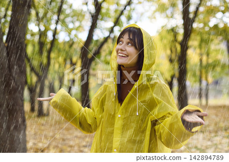 Happy young woman in yellow raincoat enjoying autumn rain in green park outdoors Happy young woman in yellow raincoat enjoying autumn rain in green park outdoors 142894789
