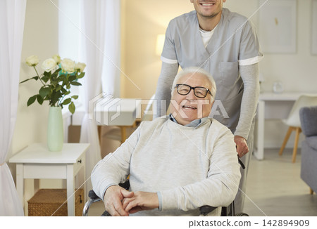 Smiling elderly man in wheelchair enjoying time at home with caregiver offering support and care. Smiling elderly man in wheelchair enjoying time at home with caregiver offering support and care. 142894909