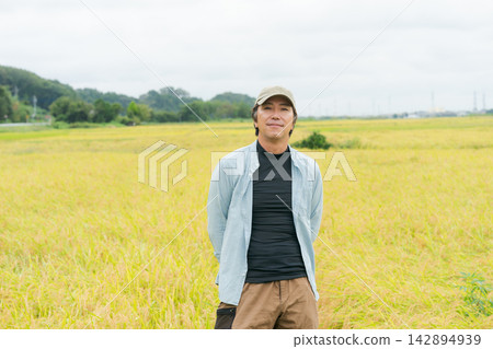 收割季節,一位農夫站在稻田前。 收割季節,一位農夫站在稻田前。 142894939