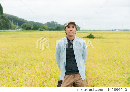 收割季節,一位農夫站在稻田前。 收割季節,一位農夫站在稻田前。 142894940