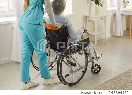 Doctor Or Nurse Moving Elderly Patient In Wheelchair During Rehabilitation Doctor Or Nurse Moving Elderly Patient In Wheelchair During Rehabilitation 142894985