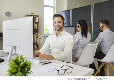 Confident male call center agent with headset working at modern office desk 142895500