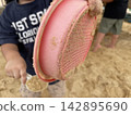 孩子的雙手展示著一個沾滿沙子的粉紅色篩子。 142895690