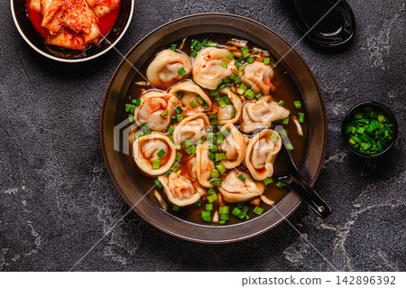Dumplings served in a bowl with broth and green onions. 142896392
