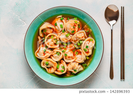 Dumplings served in a bowl with broth and green onions. 142896393