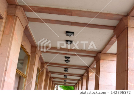 Architectural Symmetry in a Columned Walkway with Stone Pillars and Ceiling Lights 142896572