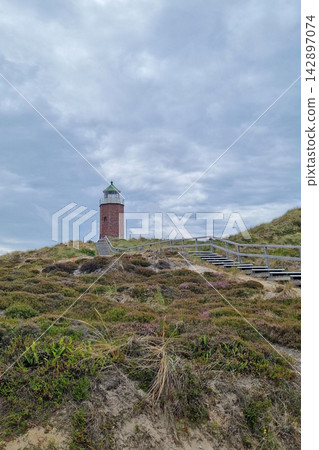 Coastal Lighthouse and Sandy Dunes Under Overcast Skies for Nautical Themed Design Coastal Lighthouse and Sandy Dunes Under Overcast Skies for Nautical Themed Design 142897074