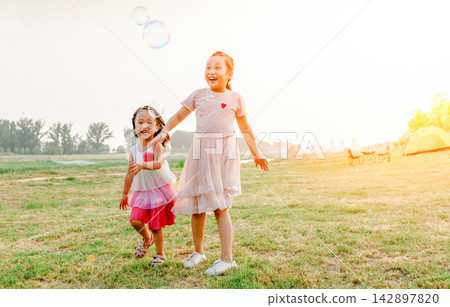 Happy family playing with bubbles by orange tent during summer camping trip in countryside. Happy family playing with bubbles by orange tent during summer camping trip in countryside. 142897820