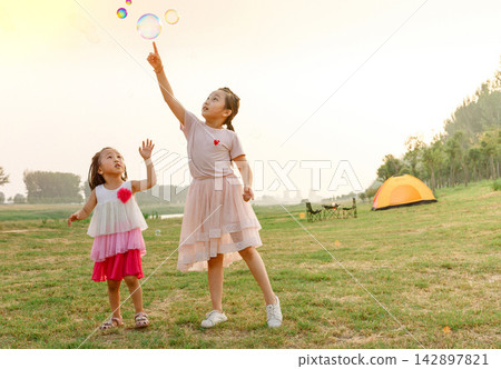 Happy family playing with bubbles by orange tent during summer camping trip in countryside. 142897821