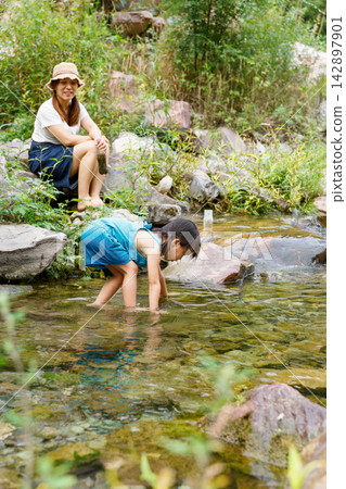 Happy family playing in the clear mountain river during summer trip Happy family playing in the clear mountain river during summer trip 142897901
