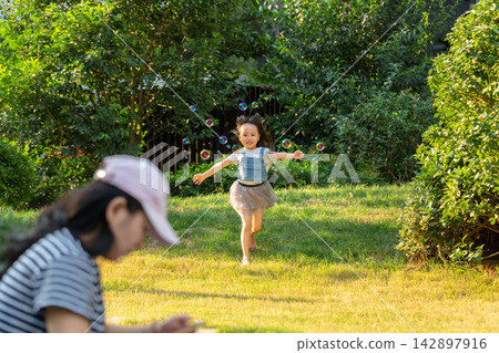 Little girl playing with bubbles in park while parent using smartphone, modern parenting and screen distraction concept Little girl playing with bubbles in park while parent using smartphone, modern parenting and screen distraction concept 142897916