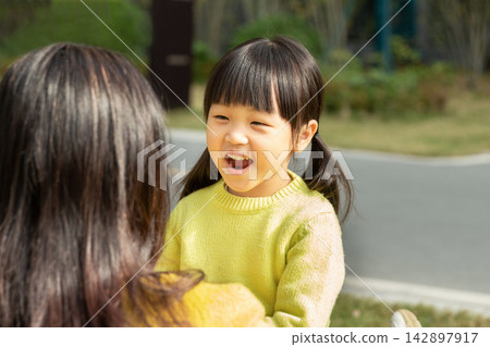 Affectionate Asian mother and daughter sitting on grass and laughing together, emotional connection and family happiness. 142897917