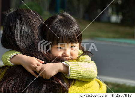 Little Asian girl giving a tight hug to her mother outdoors, showing love and security. 142897918