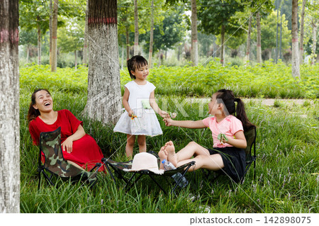 Mother and little daughter sitting on grass and drinking water during picnic in the forest Mother and little daughter sitting on grass and drinking water during picnic in the forest 142898075