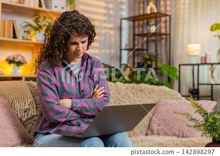 Young woman on home sofa reacting to bad laptop news with stress after job interview failure indoors Young woman on home sofa reacting to bad laptop news with stress after job interview failure indoors 142898297