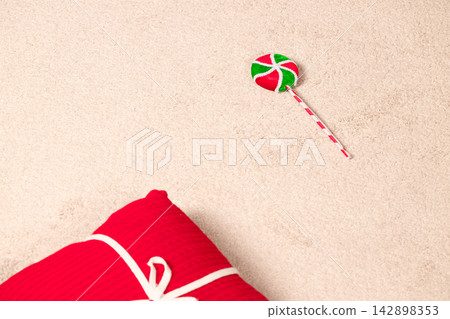 Festive Christmas lollipop and a wrapped red gift box on a soft textured neutral background 142898353