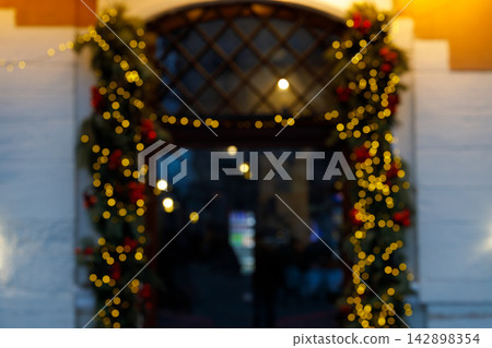 Blurred Christmas entrance with glowing golden fairy lights and festive holiday garland decor 142898354