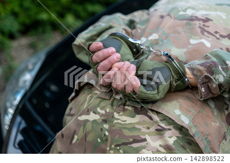 Detained military man lies against a vehicle with his restrained hands behind his back after arrest. Detained military man lies against a vehicle with his restrained hands behind his back after arrest. 142898522