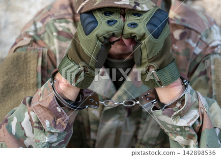 Handcuffs on raised hands of captive serviceman in close up Handcuffs on raised hands of captive serviceman in close up 142898536