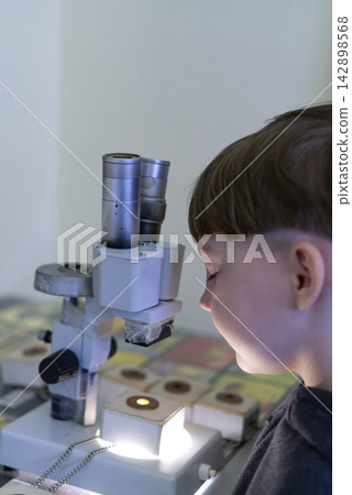 Curious boy looking through a microscope at a science exhibition or museum Curious boy looking through a microscope at a science exhibition or museum 142898568